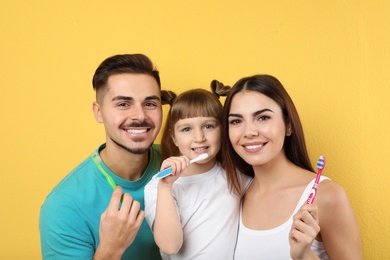 Photo of Little girl and her parents brushing teeth together on color background