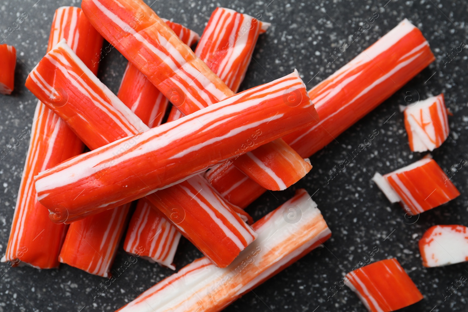 Photo of Delicious crab sticks on black board, flat lay