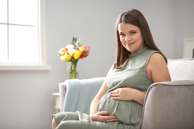 Beautiful pregnant woman sitting in armchair at home