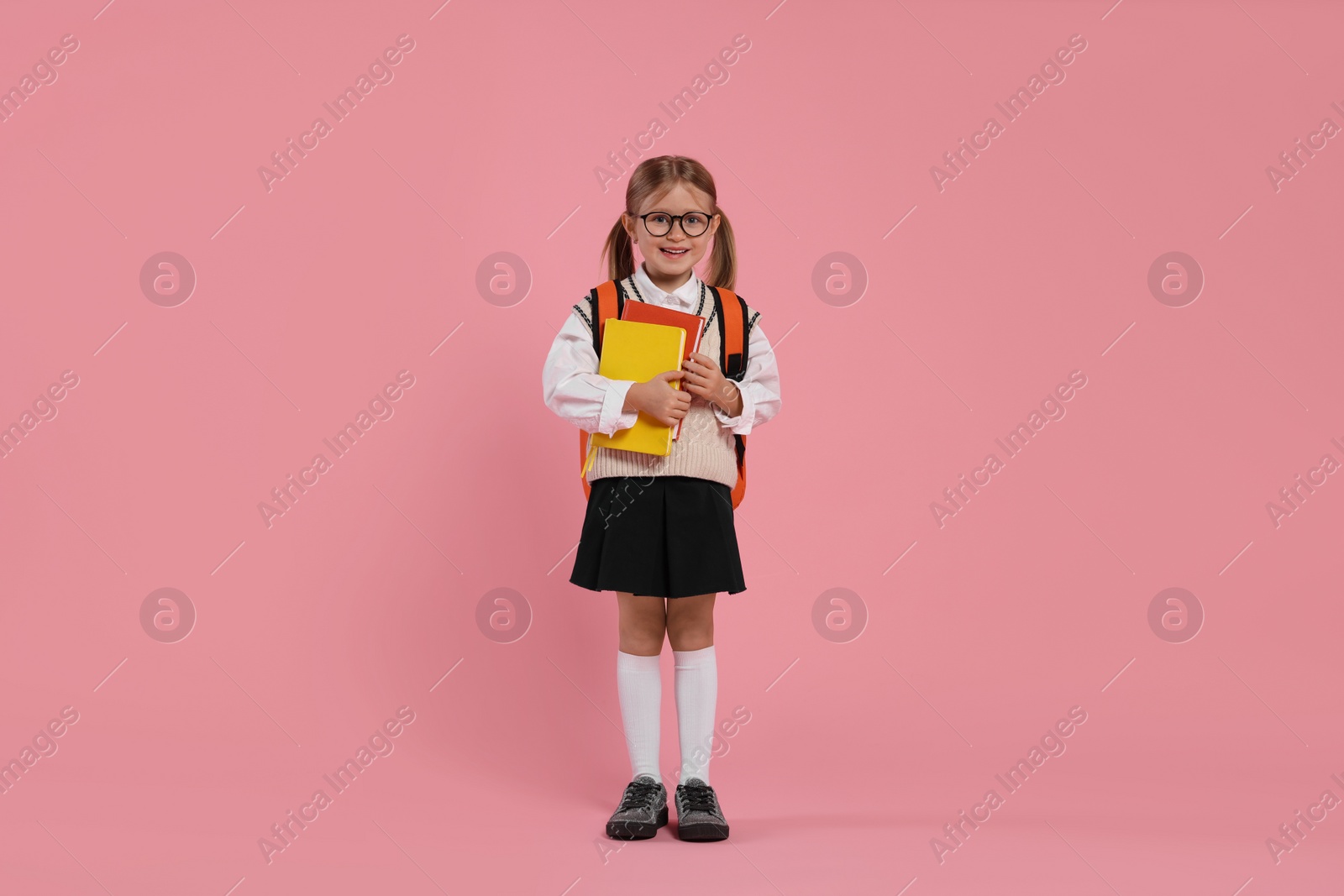 Photo of Happy schoolgirl in glasses with backpack and books on pink background