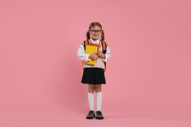 Photo of Happy schoolgirl in glasses with backpack and books on pink background