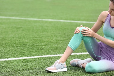 Woman in sportswear suffering from knee pain at soccer field, closeup