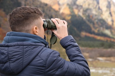 Photo of Boy looking through binoculars in beautiful mountains, back view