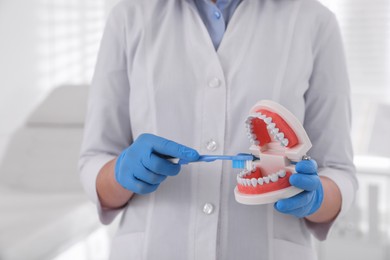 Photo of Dentist with jaws model and toothbrush in clinic, closeup. Oral care demonstration