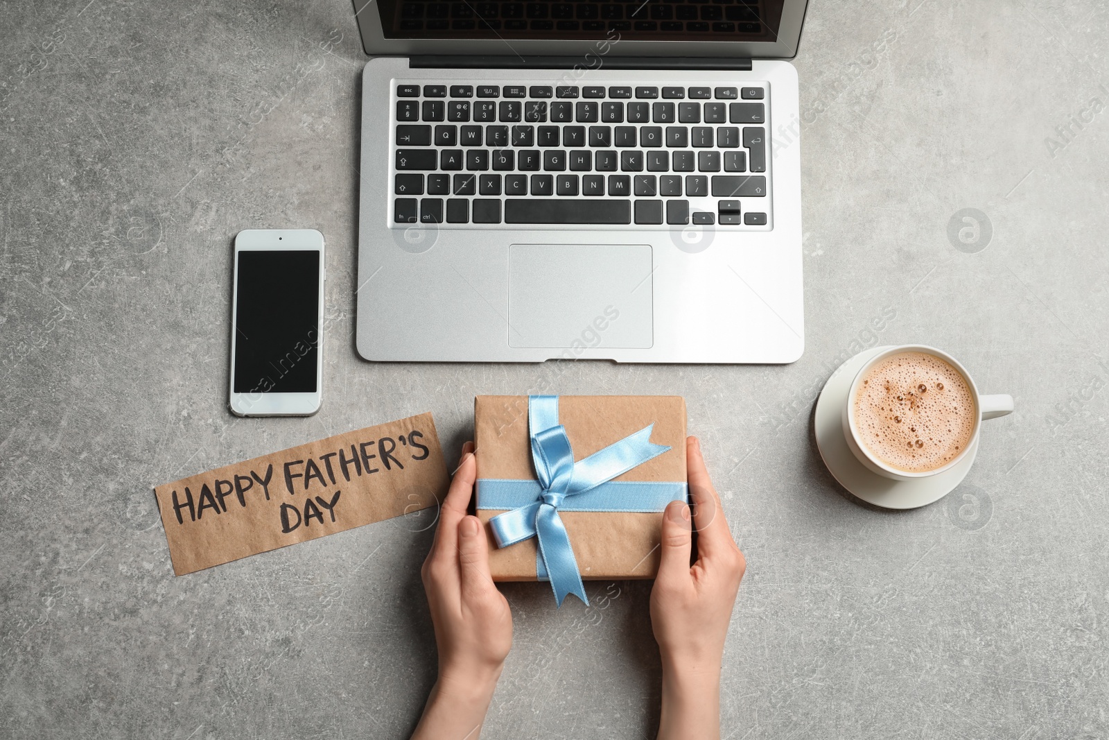 Photo of Man holding gift box near smartphone and laptop on table, top view. Father's day celebration