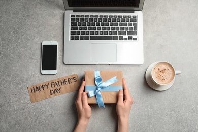 Man holding gift box near smartphone and laptop on table, top view. Father's day celebration