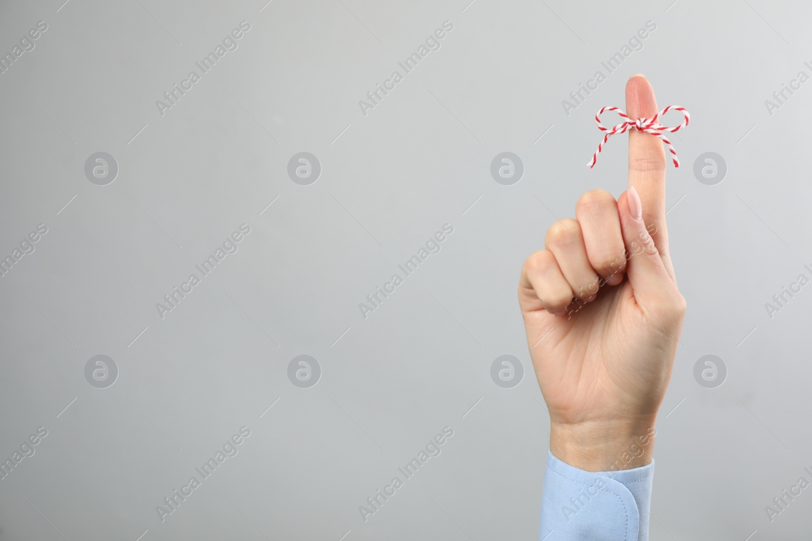 Photo of Woman showing index finger with tied bow as reminder on light grey background, closeup. Space for text