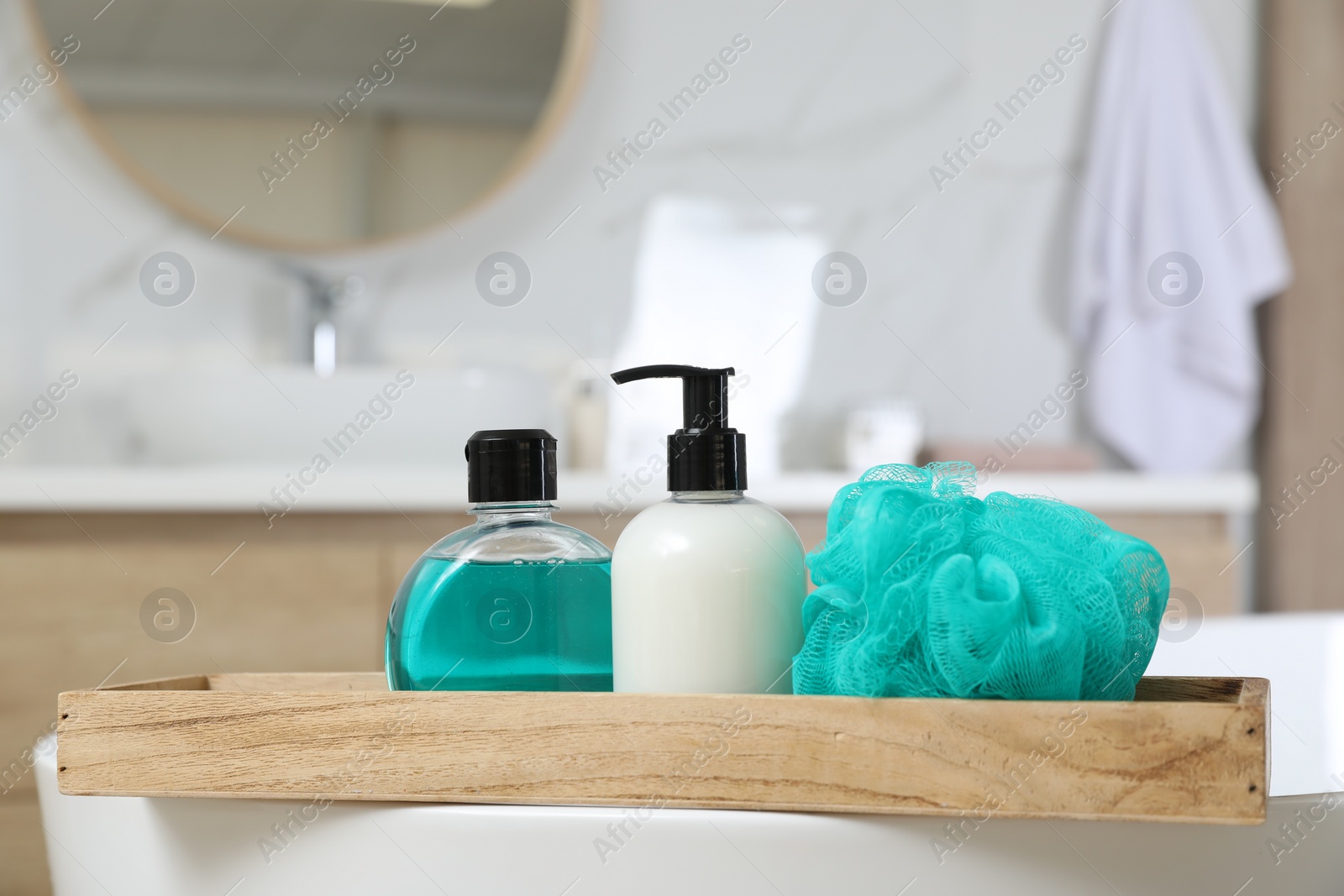 Photo of Wooden bath tray with bottles of shower gels and mesh pouf on tub indoors