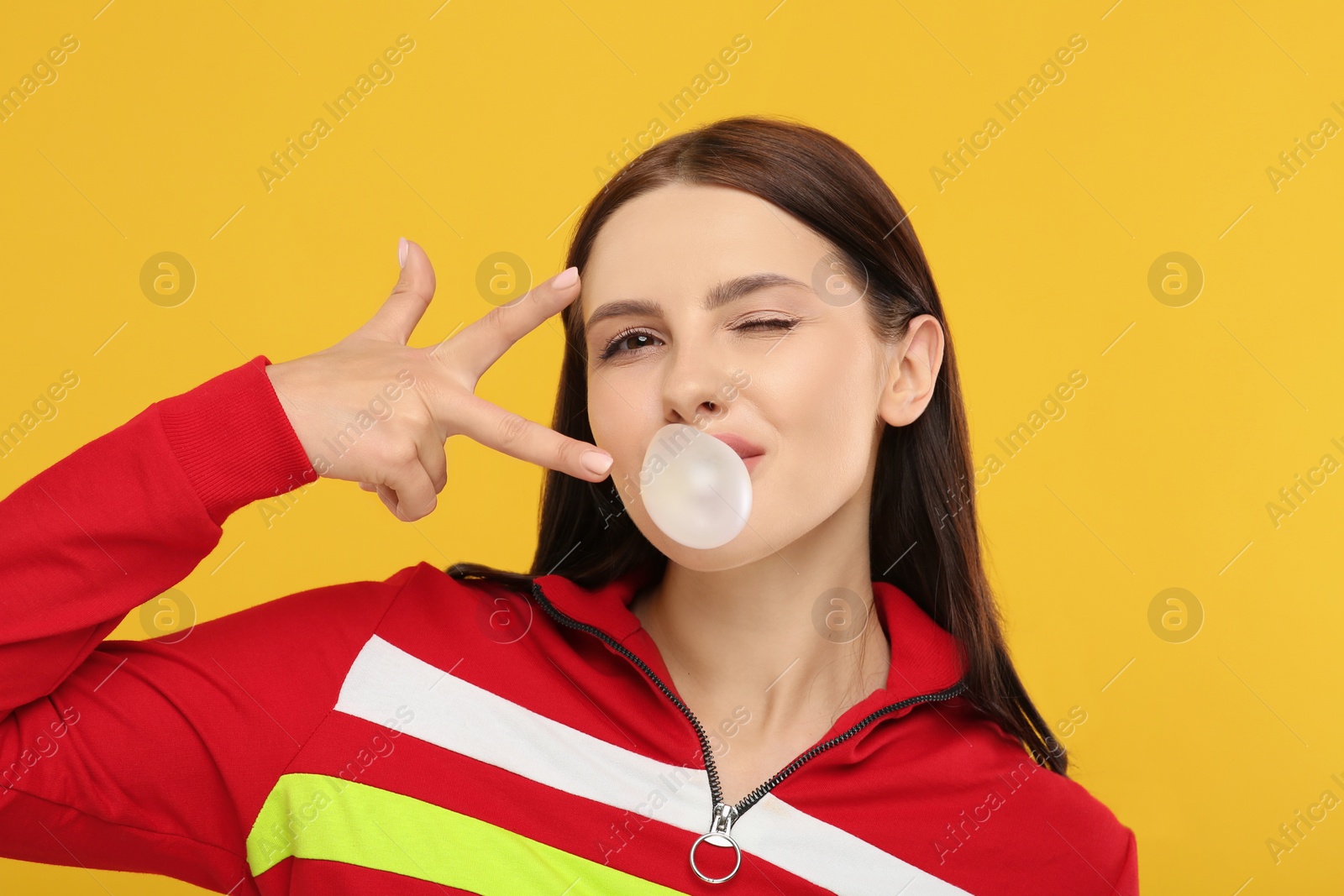 Photo of Beautiful woman blowing bubble gum and gesturing on orange background