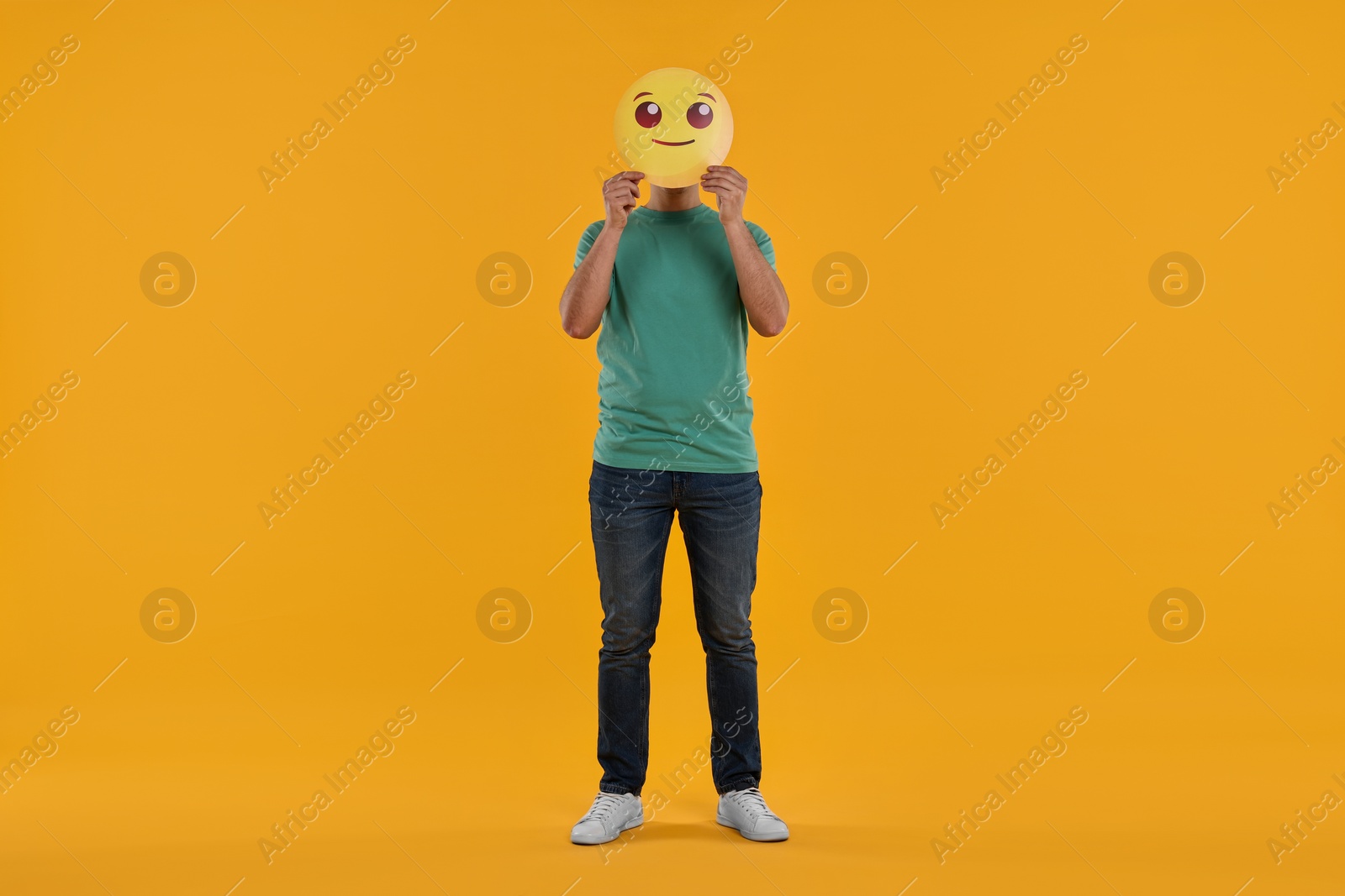 Photo of Man covering face with smiling emoticon on yellow background