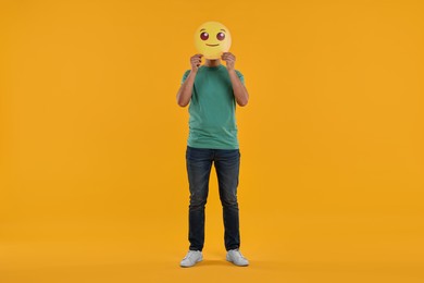 Man covering face with smiling emoticon on yellow background