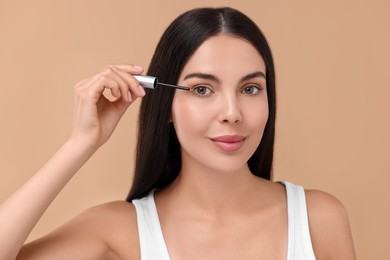 Photo of Beautiful woman applying serum onto her eyelashes on beige background. Cosmetic product
