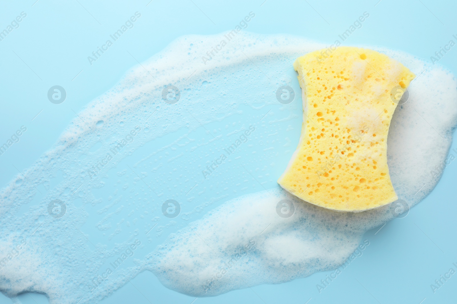 Photo of Yellow sponge with foam on light blue background, top view