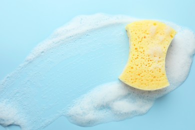 Yellow sponge with foam on light blue background, top view