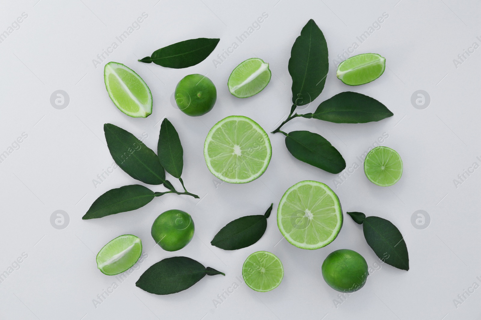 Photo of Whole and cut fresh limes with leaves on white background, flat lay