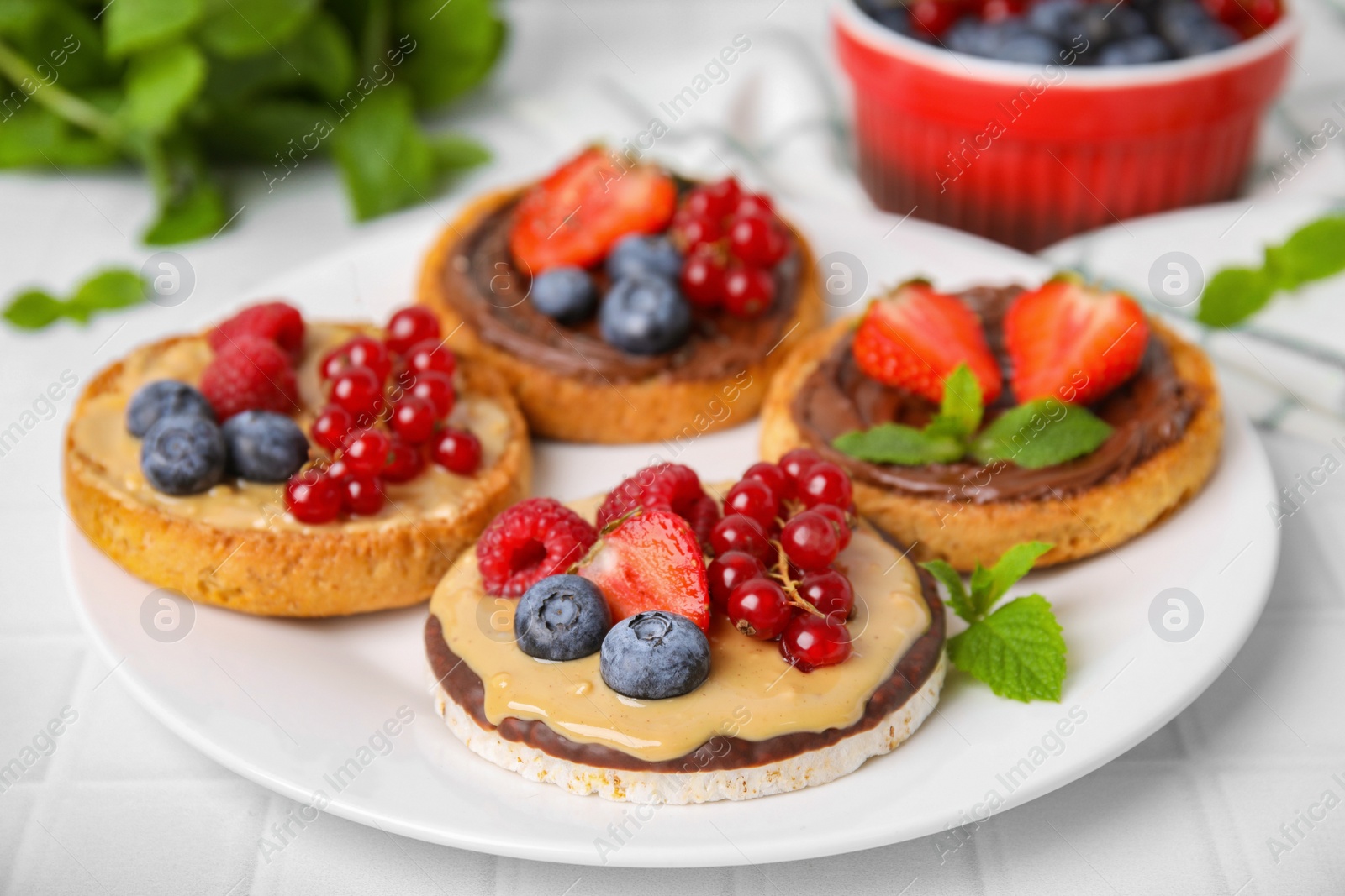 Photo of Fresh rice cake and rusks with different toppings served on white table, closeup