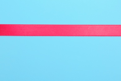 Photo of Simple pink ribbon on color background, top view