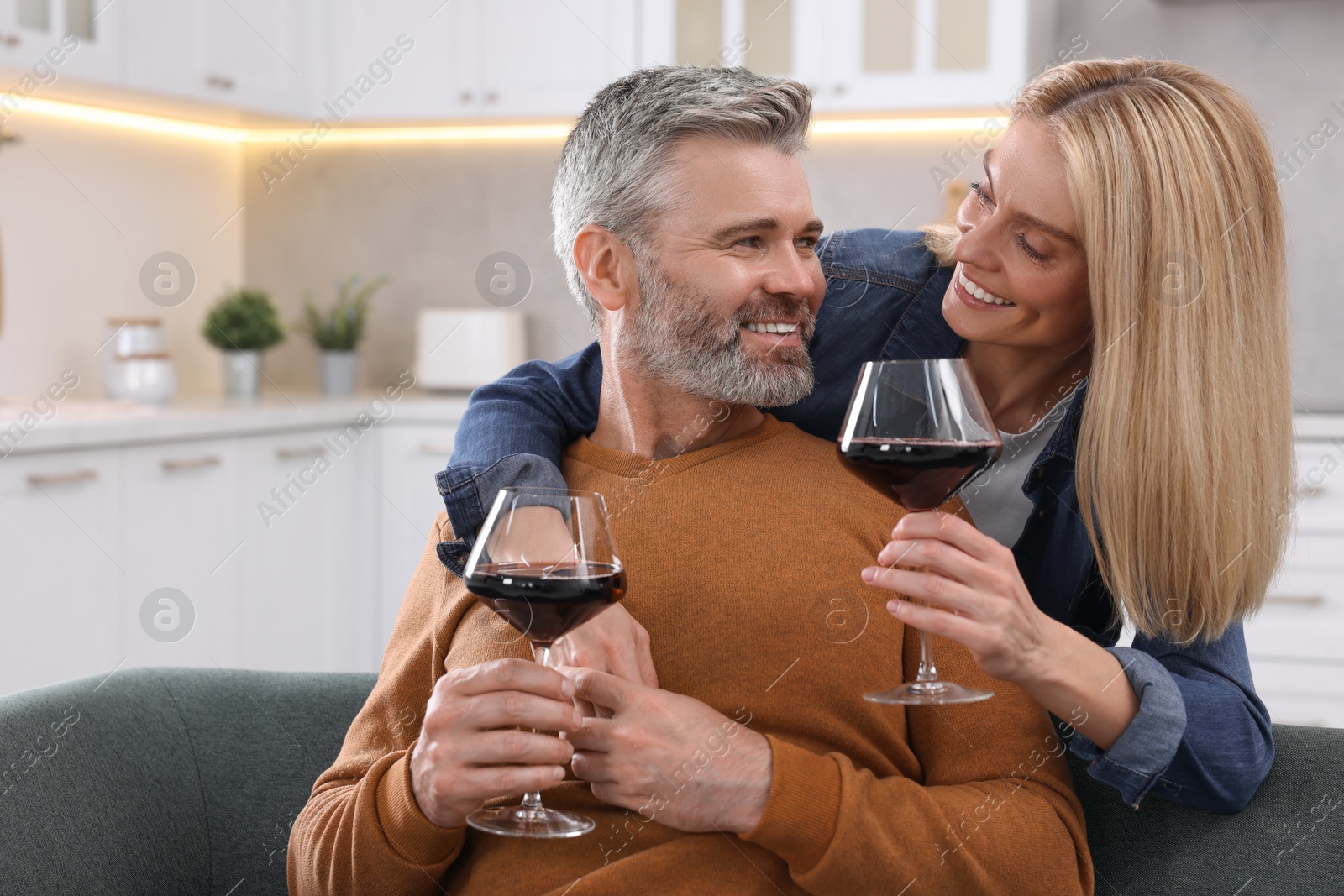 Photo of Happy affectionate couple with glasses of wine on sofa at home, space for text. Romantic date