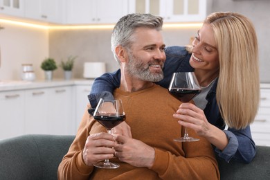 Photo of Happy affectionate couple with glasses of wine on sofa at home, space for text. Romantic date