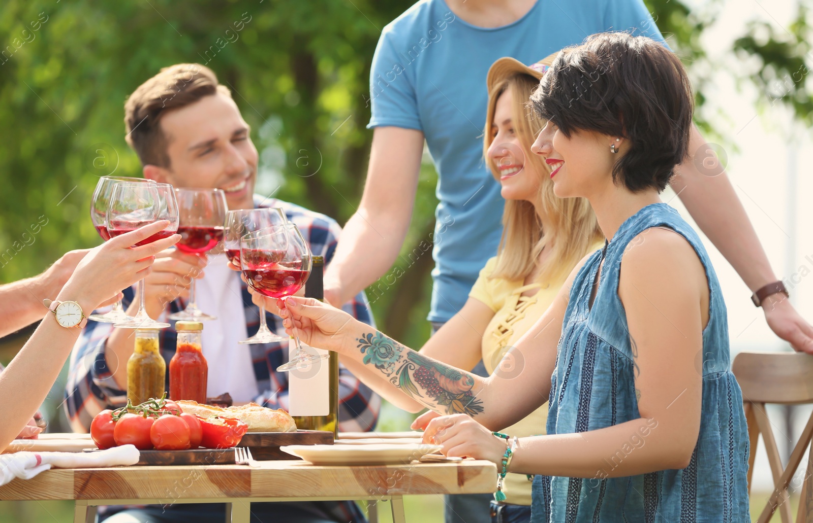 Photo of Young people with glasses of wine at table outdoors. Summer barbecue