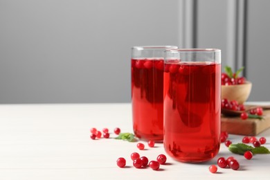 Photo of Tasty cranberry juice in glasses and fresh berries on white wooden table, space for text