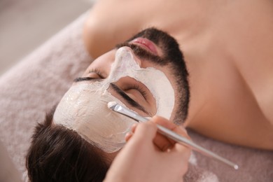 Cosmetologist applying mask on man's face in spa salon