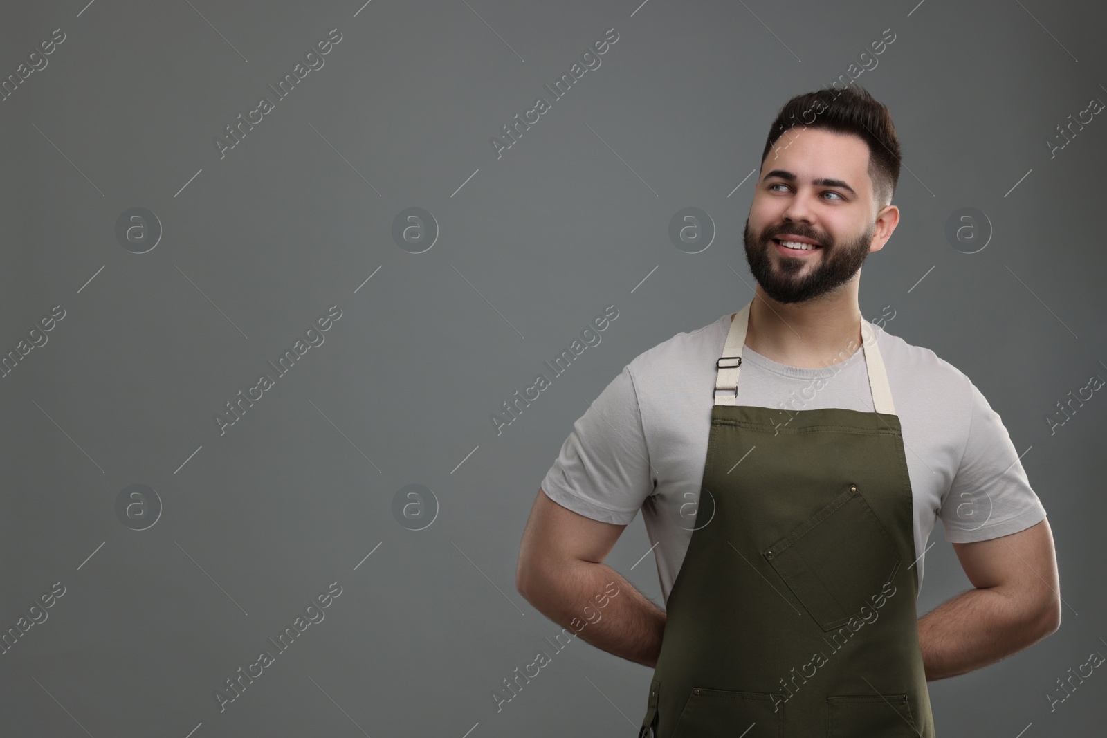 Photo of Smiling man in kitchen apron on grey background. Mockup for design