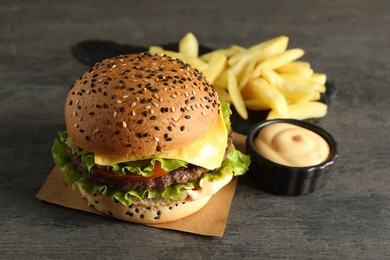 Photo of Burger with delicious patty, french fries and sauce on gray table