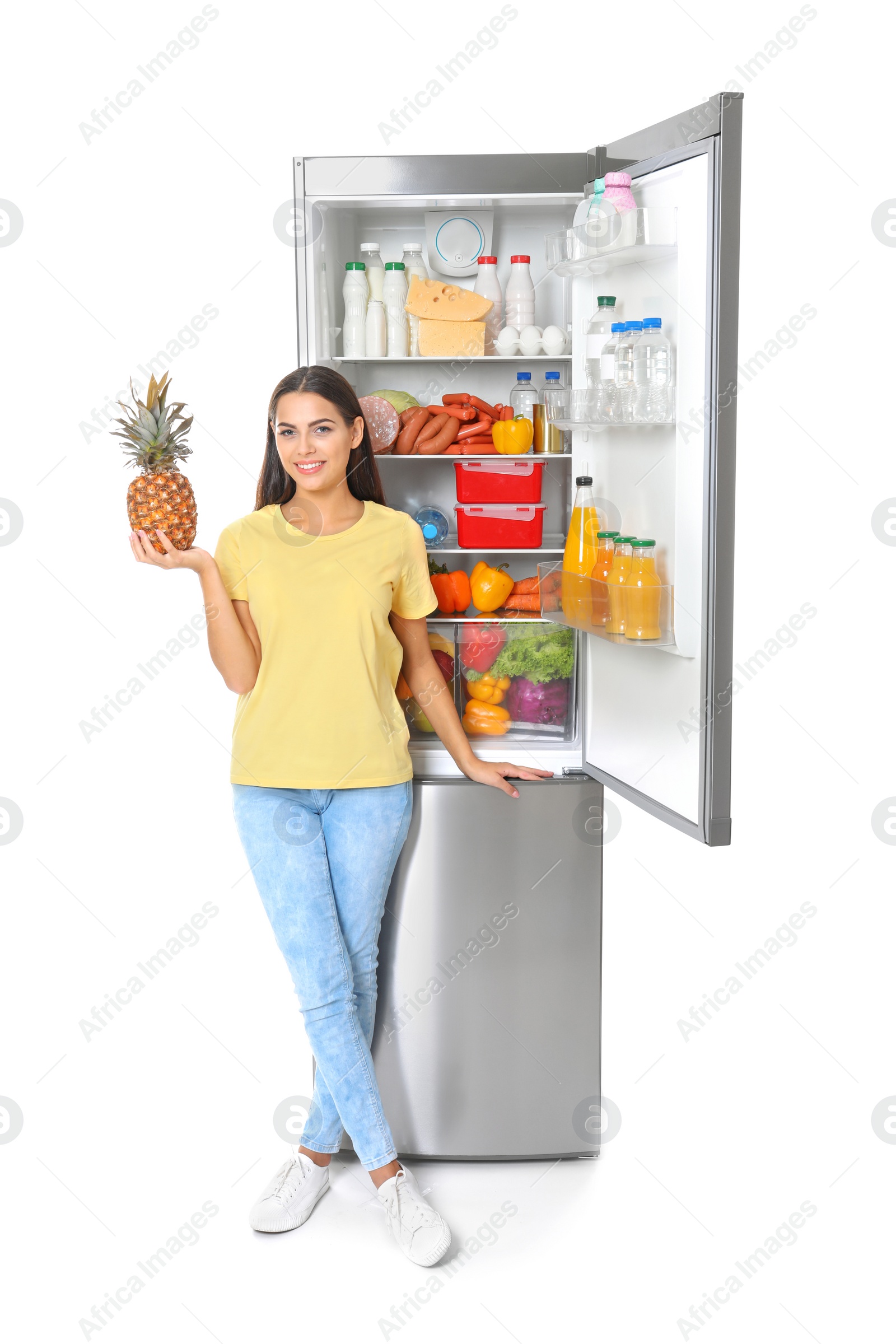 Photo of Young woman with pineapple near open refrigerator on white background