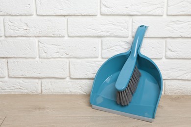 Photo of Plastic whisk broom with dustpan near white brick wall indoors. Space for text