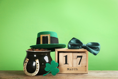 Photo of Composition with pot of gold coins and wooden block calendar on table against green background. St. Patrick's Day celebration