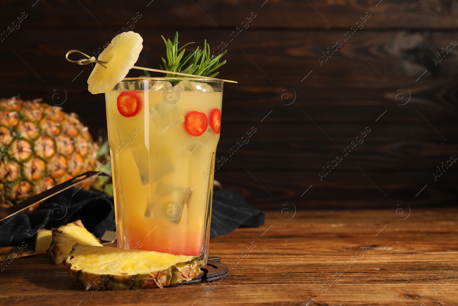 Photo of Spicy pineapple cocktail with chili pepper, rosemary and fresh fruit on wooden table. Space for text