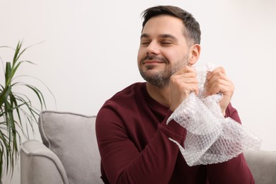 Happy man with bubble wrap indoors. Space for text
