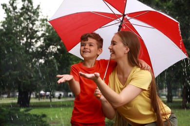 Mother and son with umbrella walking under rain in park