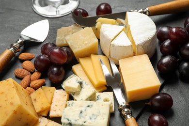 Photo of Cheese platter with specialized knives and fork on black table, closeup view