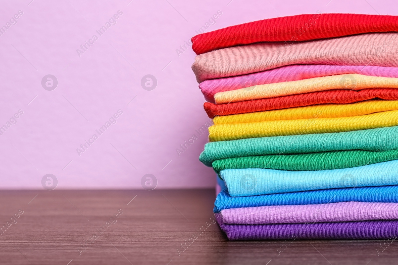 Photo of Stack of colorful t-shirts on table against color background