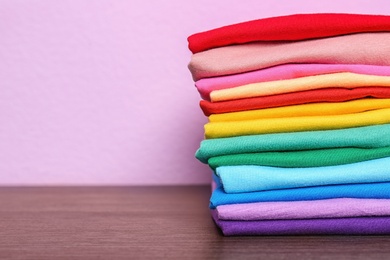 Photo of Stack of colorful t-shirts on table against color background