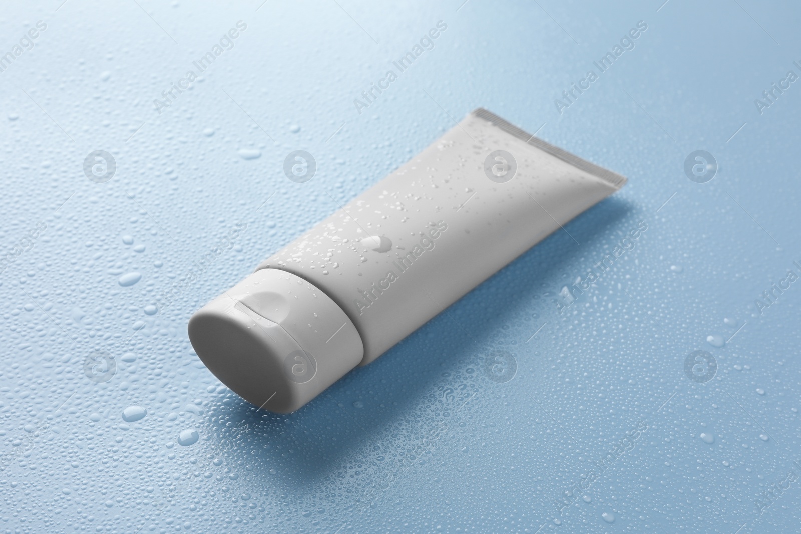 Photo of Moisturizing cream in tube on light blue background with water drops, closeup