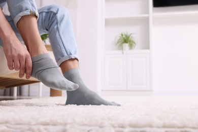 Photo of Man putting on grey socks at home, closeup. Space for text