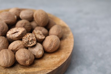 Photo of Wooden board with nutmegs on light grey table, closeup. Space for text