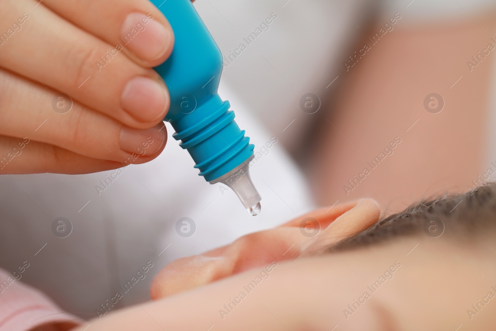 Photo of Mother dripping medication into daughter's ear on blurred background, closeup