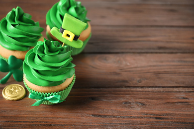 Decorated cupcakes and coins on wooden table, space for text. St. Patrick's Day celebration