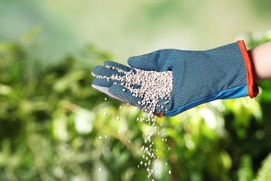 Photo of Woman in glove pouring fertilizer on blurred background, closeup with space for text. Gardening time