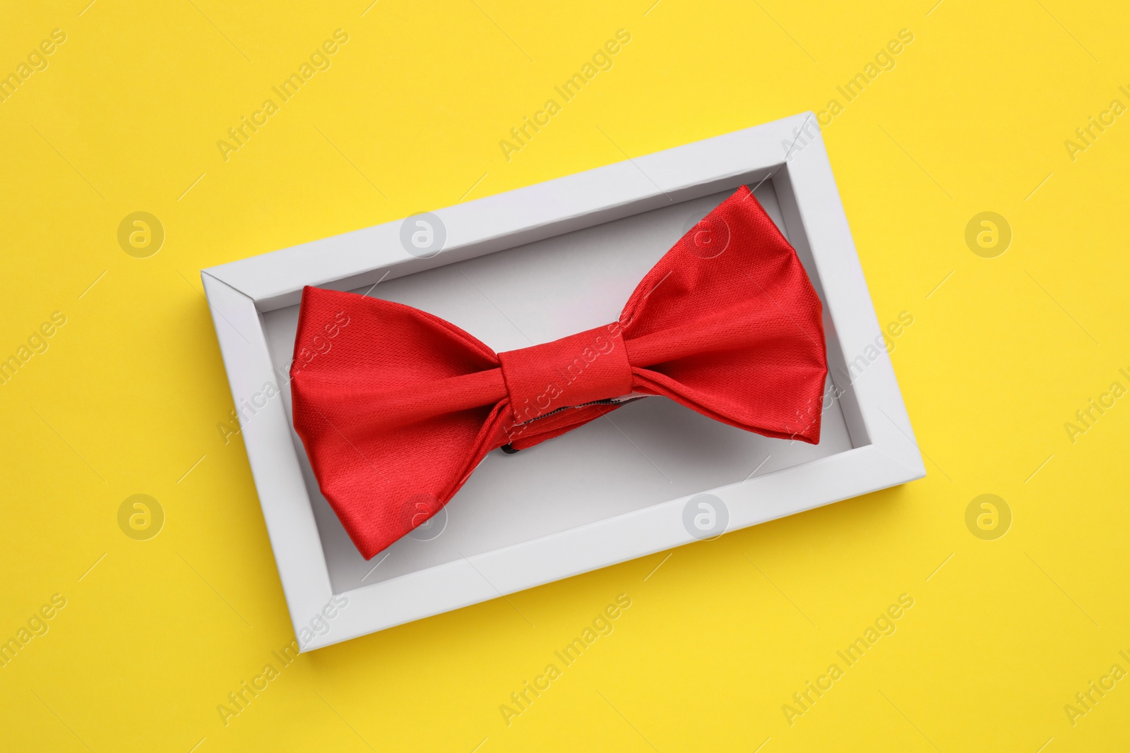 Photo of Stylish red bow tie in box on yellow background, top view