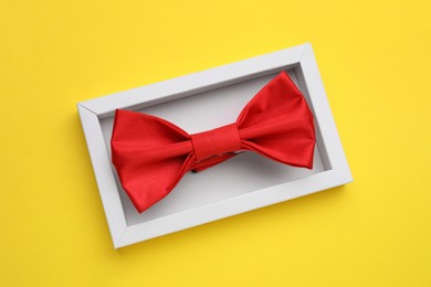 Photo of Stylish red bow tie in box on yellow background, top view