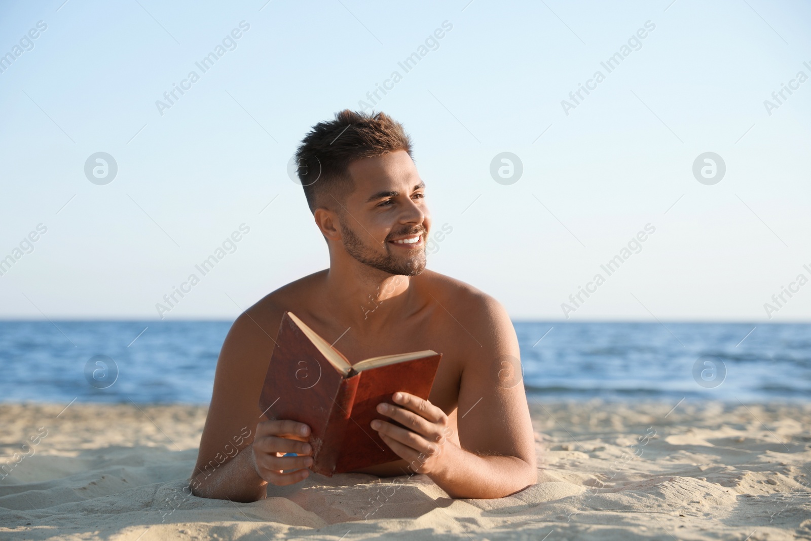 Photo of Young man reading book on sandy beach near sea