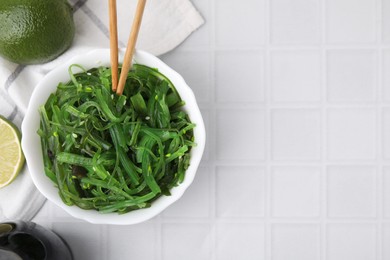 Photo of Tasty seaweed salad served in bowl on white tiled table, flat lay. Space for text
