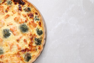 Photo of Delicious homemade quiche with salmon and broccoli on light gray marble table, top view. Space for text