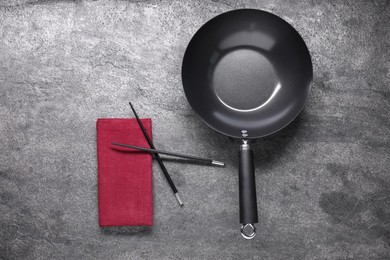 Empty iron wok and chopsticks on grey table, flat lay