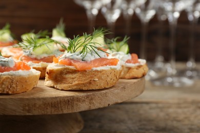 Tasty canapes with salmon, cucumber, cream cheese and dill on wooden table, closeup. Space for text